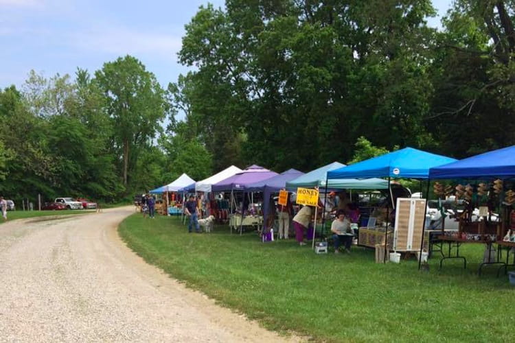Shoppers examine wares along a line of colorful vendor tents; one sign advertises honey. Shoppers examine wares along a line of colorful vendor tents; one sign advertises honey.