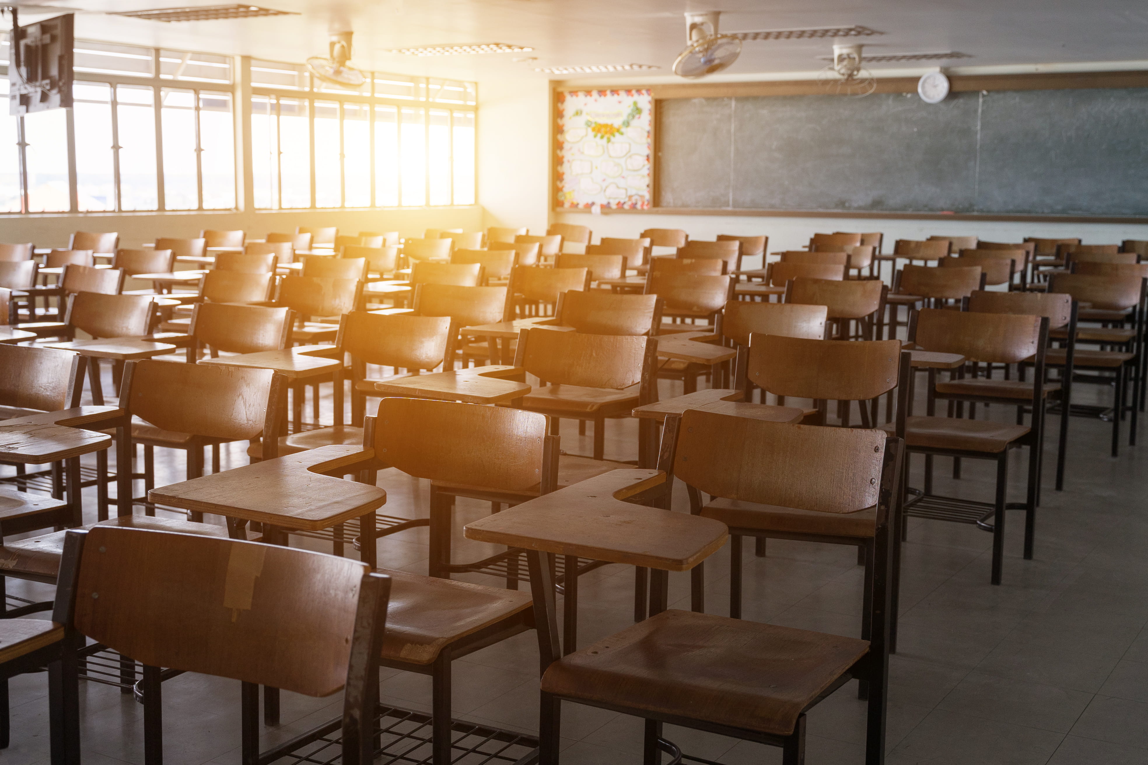 Empty grade school classroom filled with roughly 30 wooden desks and chairs