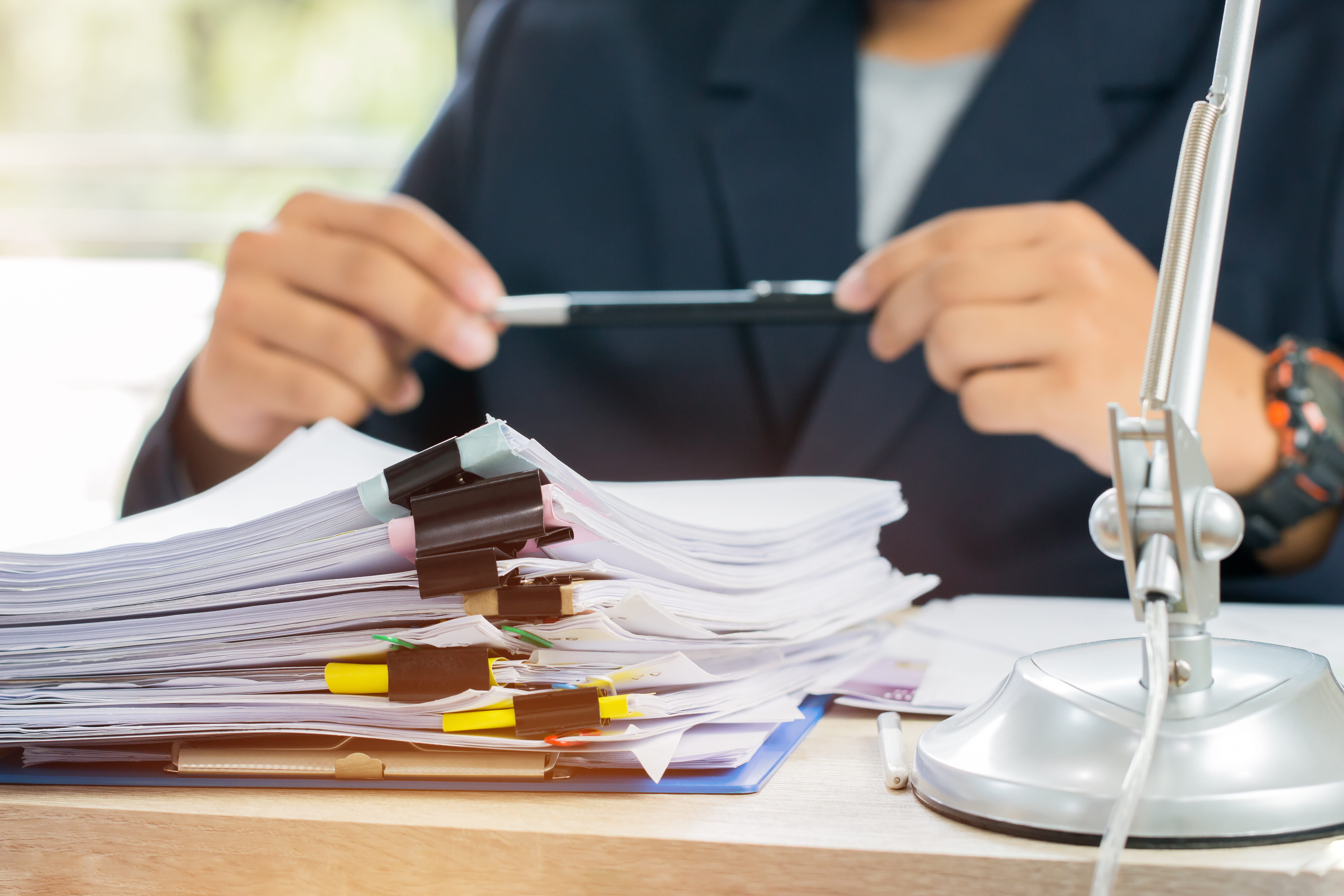 Person sitting hold pen in front of a stack of documents 