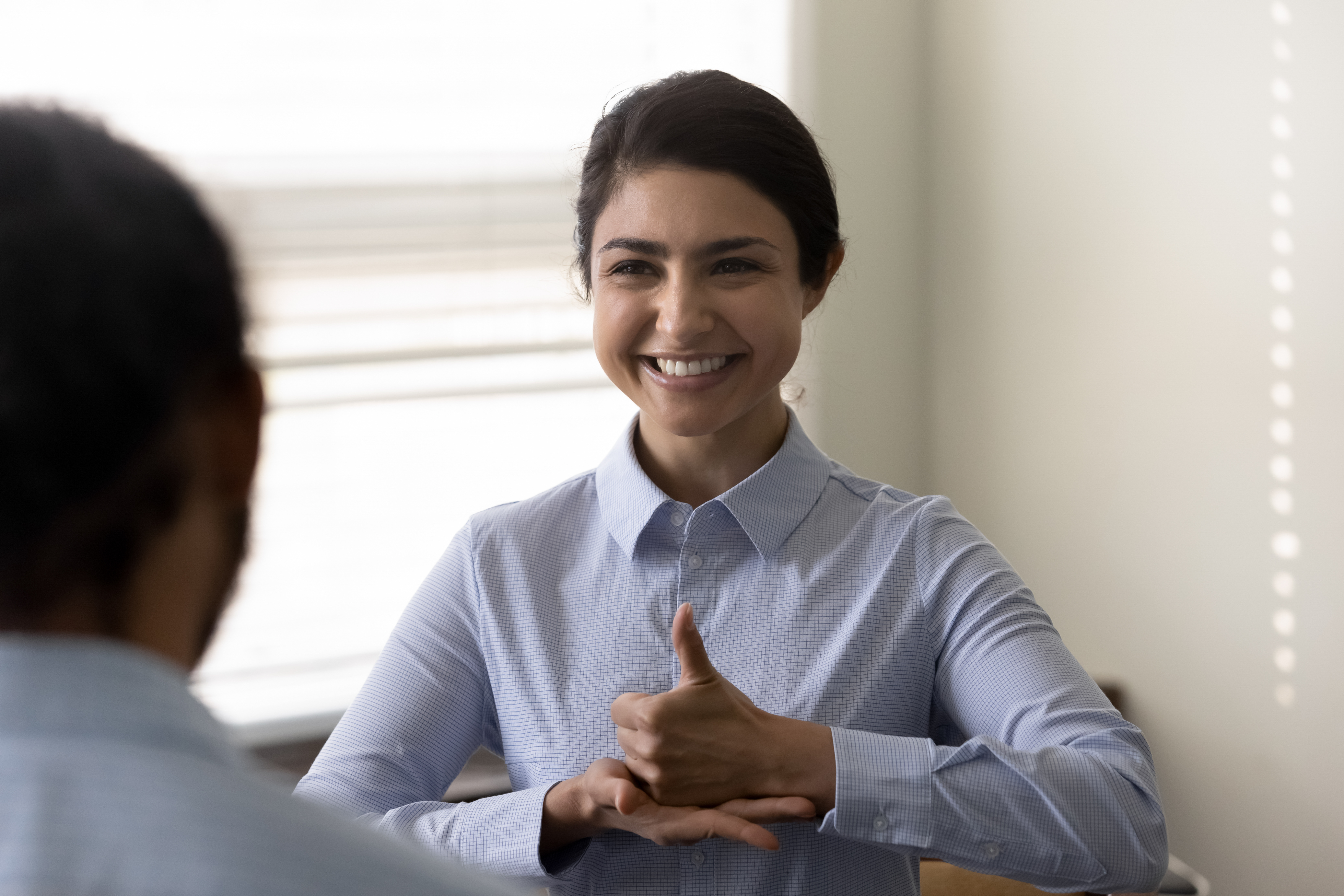 Smiling young woman using sign language to communicate with other person