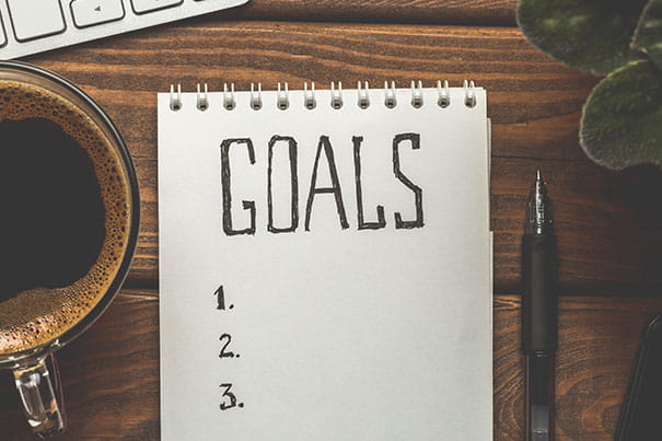 Top view of notepad with Goals List, cup of coffee on wooden table