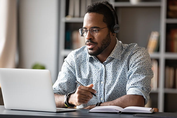Focused African-American businessman wear headphones study online watching webinar