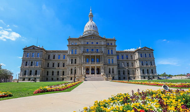The front of the Michigan State Capitol in springtime. Flower beds are filled with yellow, red, and purple flowers.