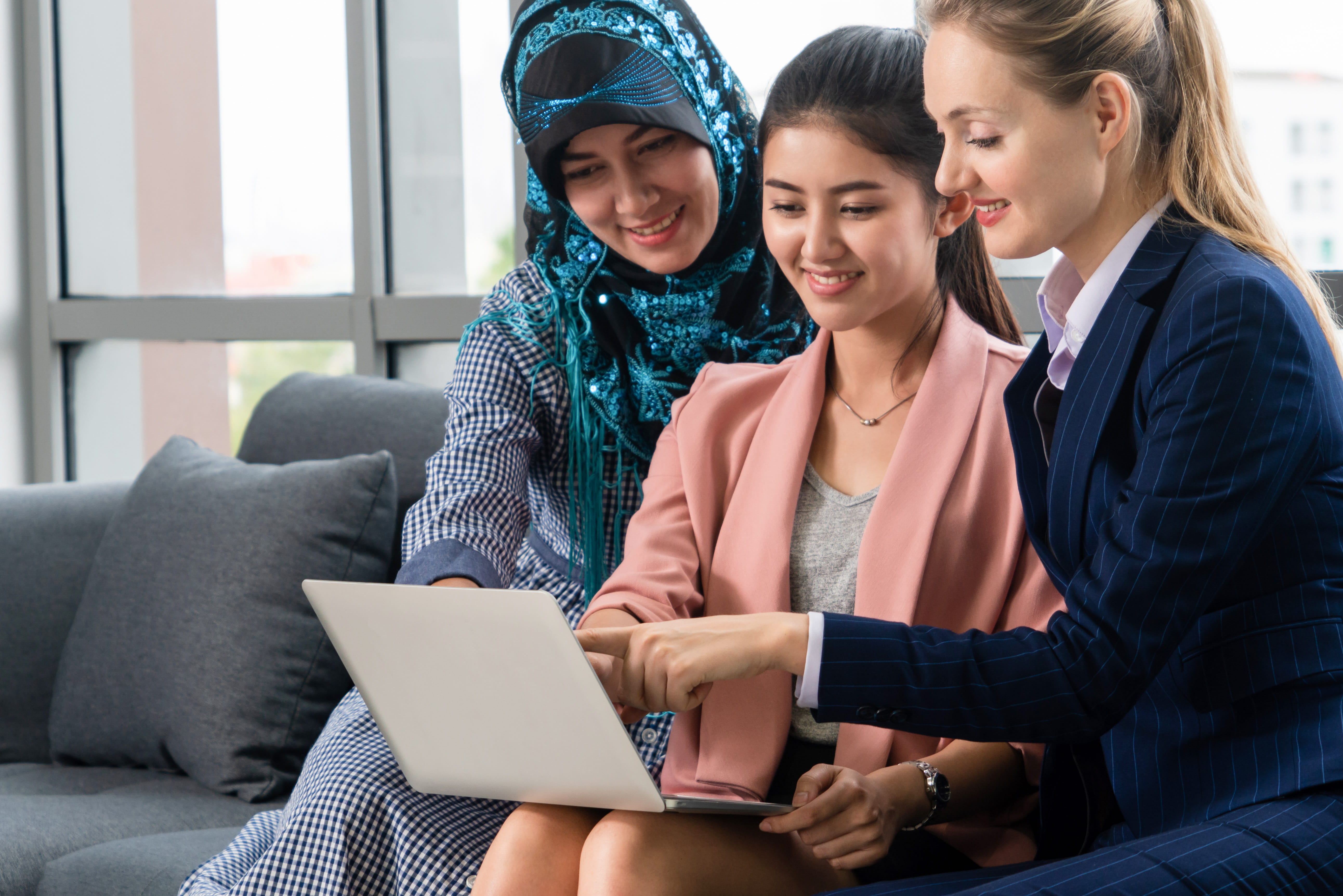 Team of businesswomen of different ethnicity, Caucasian, Asian and Arabic working together with laptop computer at office.