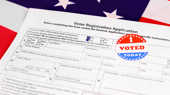 Voter application on top of U.S. flag with the "I voted" sticker pasted on top.