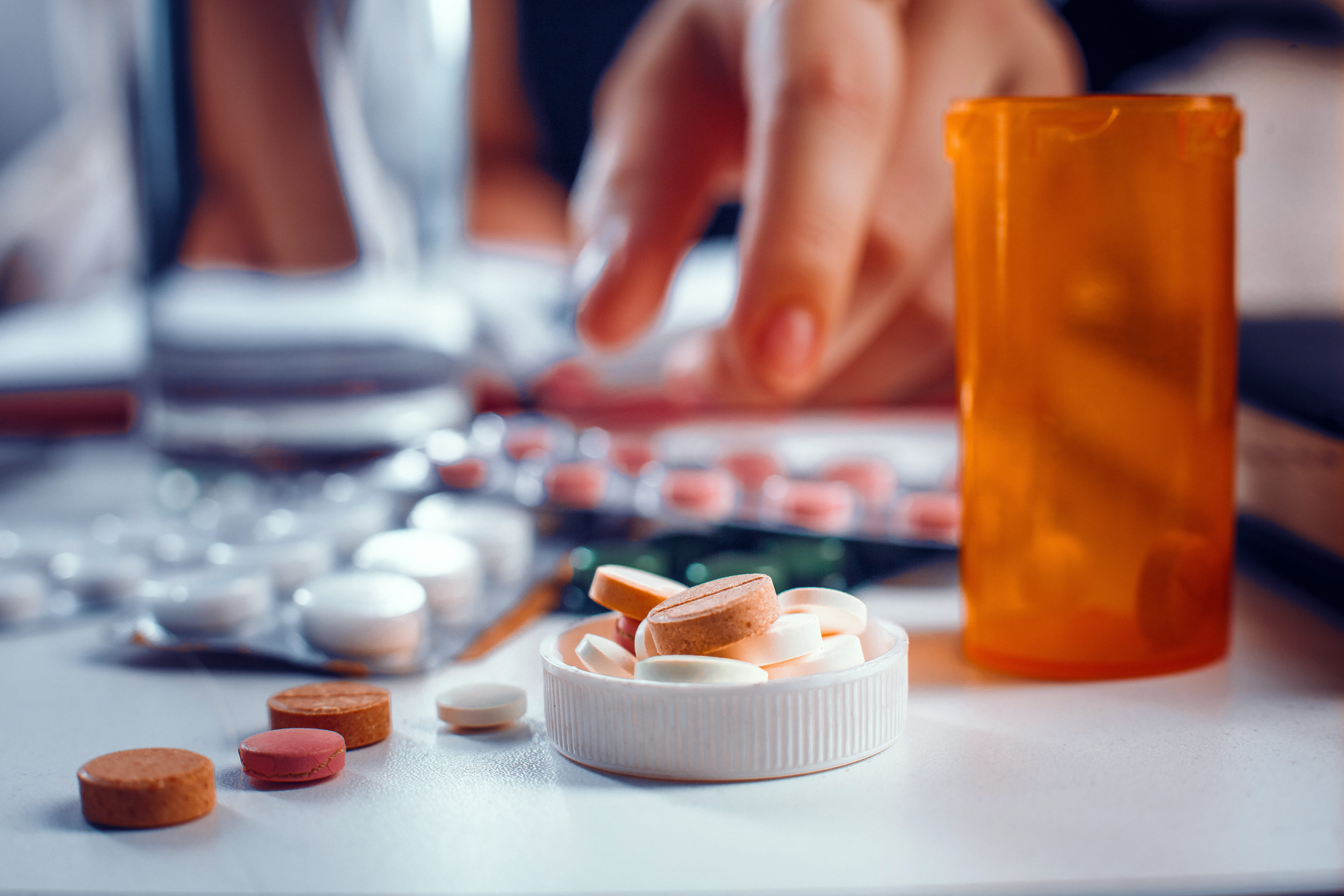Blurred hand reaches for the orange pills laying on the table