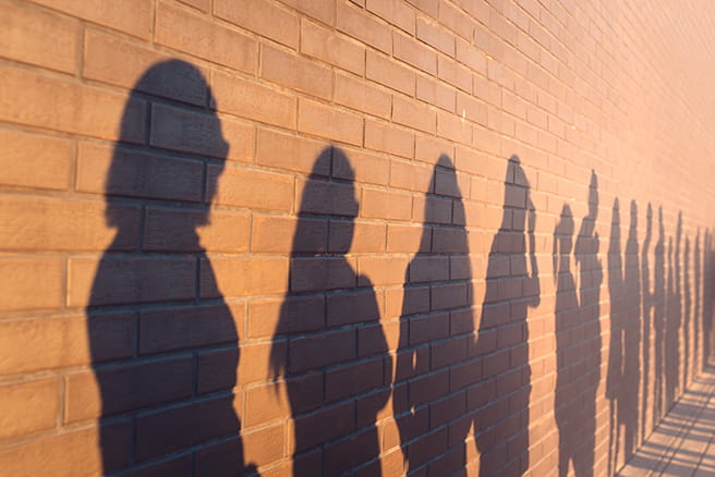 unemployment line of shadows of people lined up against a red brick wall