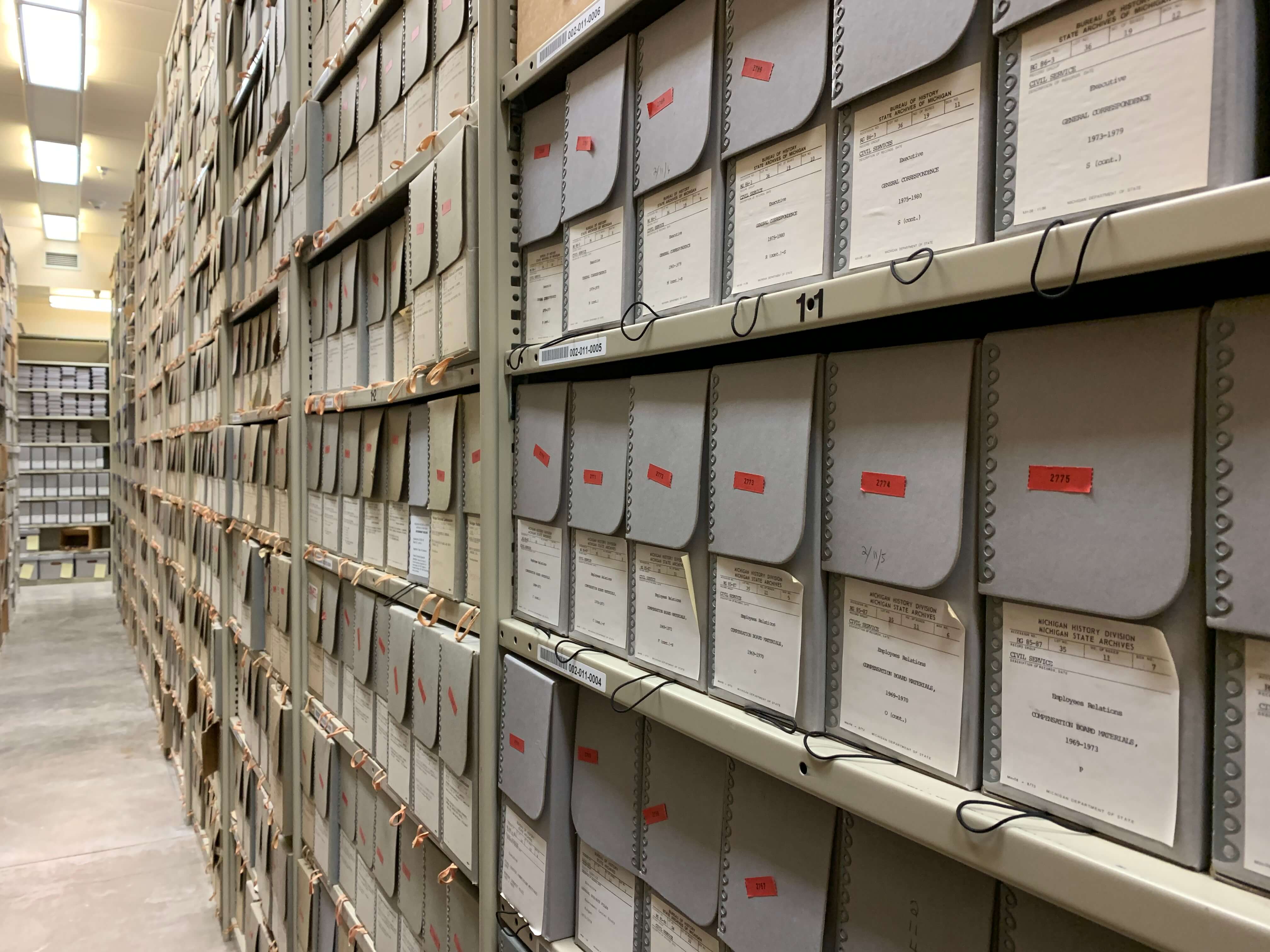 An aisle of metal shelving that holds boxes and volumes.