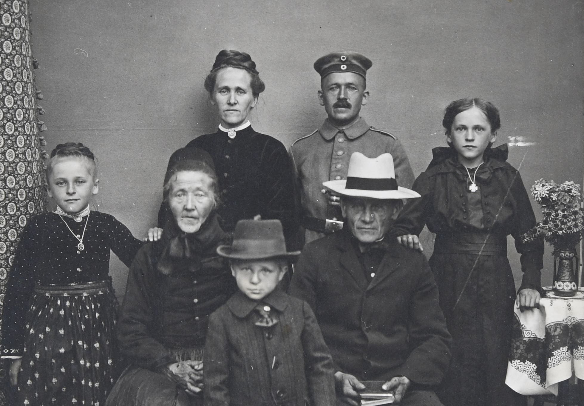 Three generations of family posing for a portrait. Grandma and grandpa are seated in the middle. Mom and dad are standing behind grandparents. Two granddaughters are standing on either side of grandparents and grandson is standing in between grandparents.
