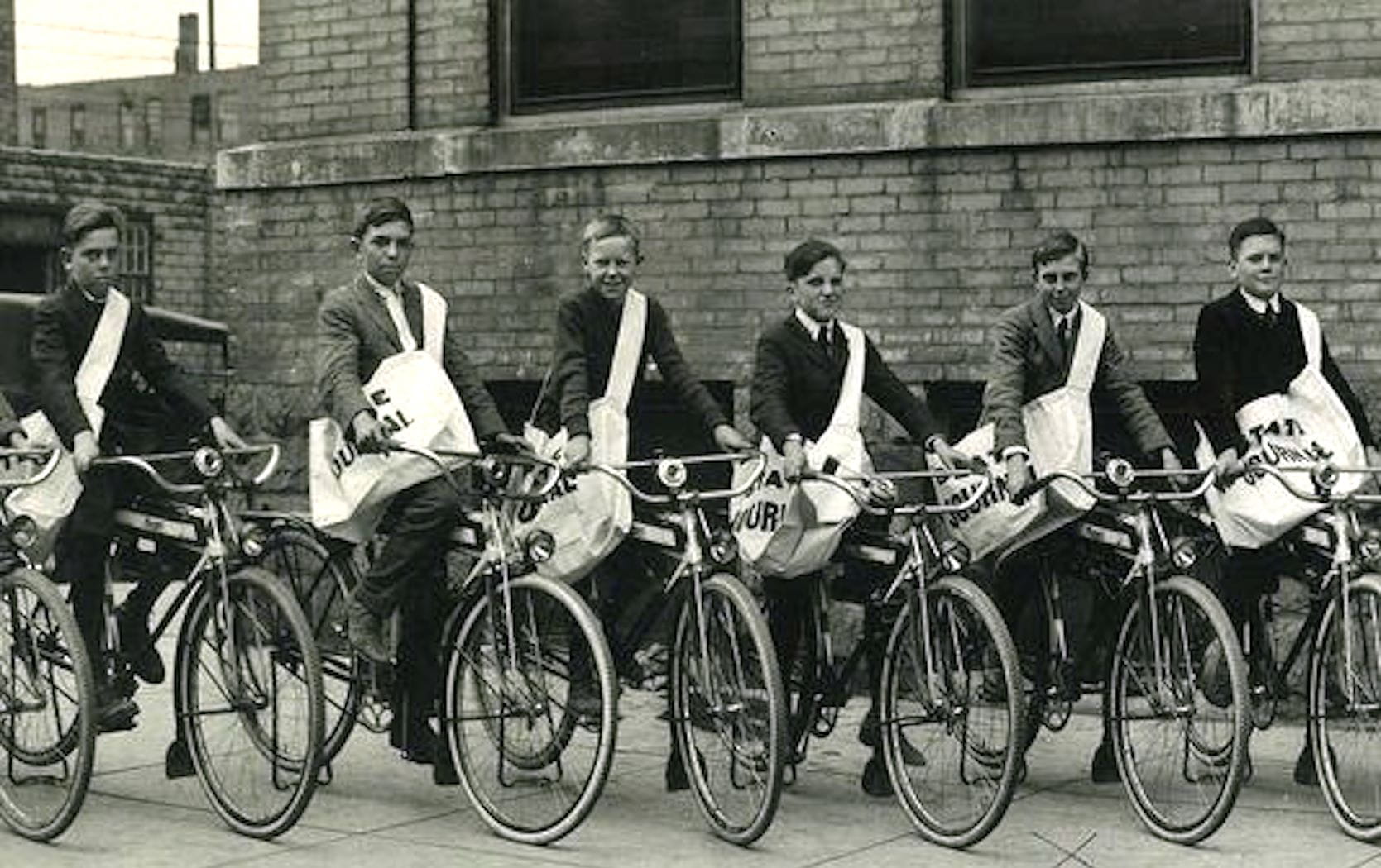 Six newspaper boys line up on their bikes.