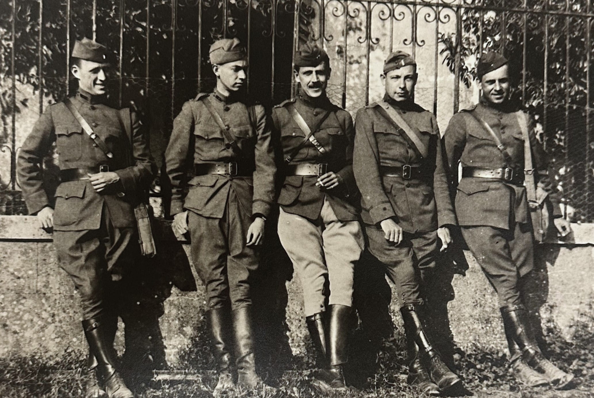 Five men in miliary gear leaning against a stone wall.