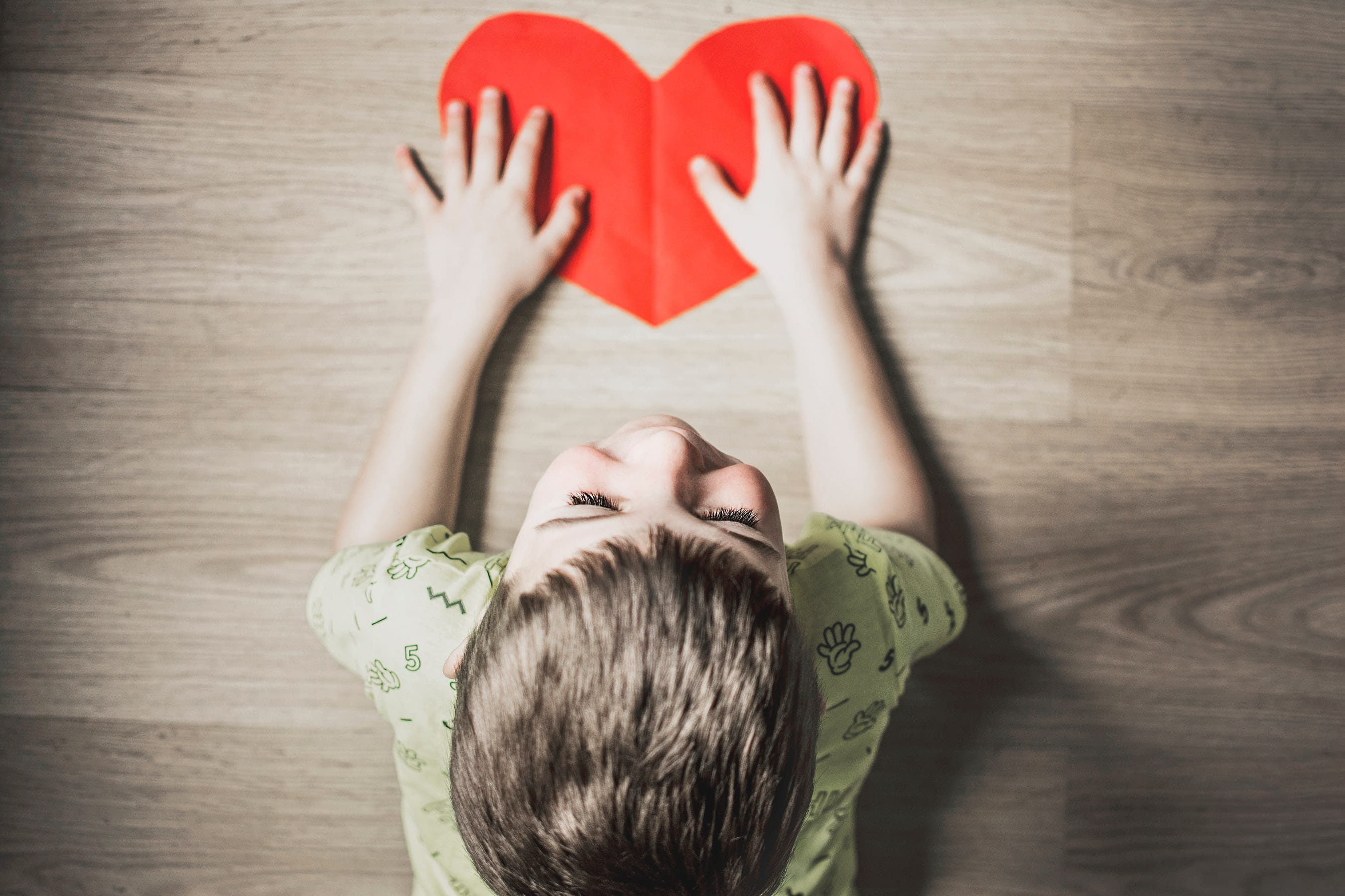 Image of a child looking down at a red paper heart