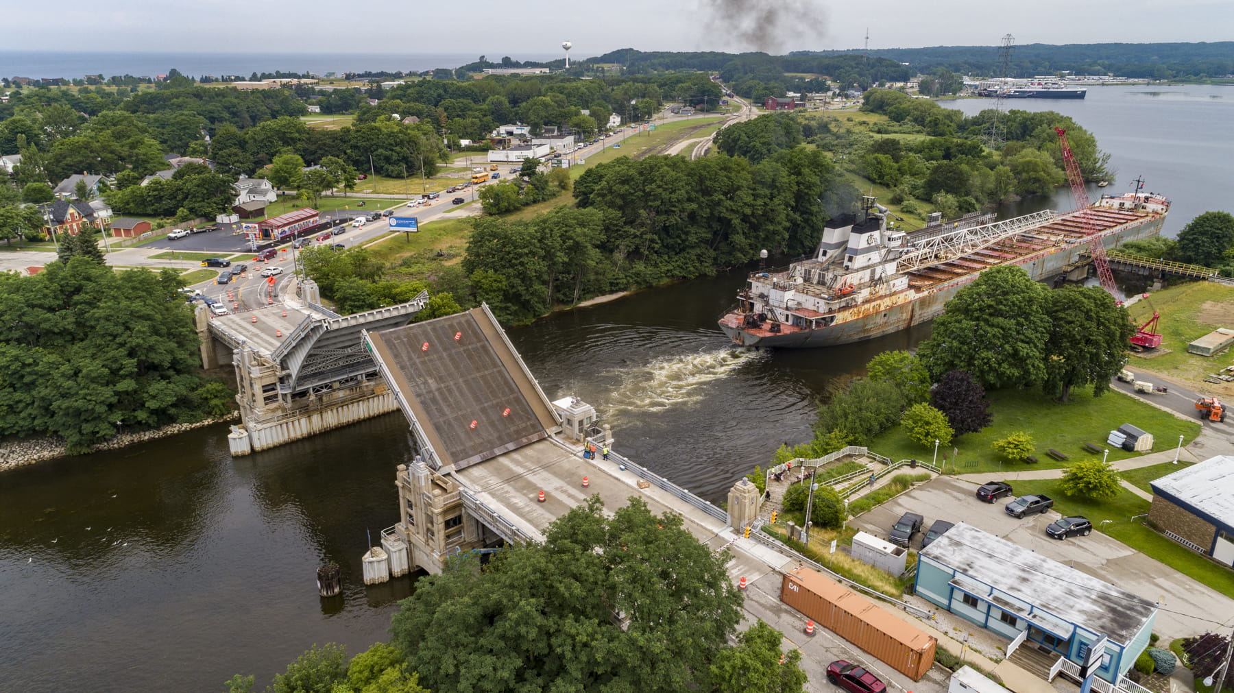 A large boat passing under a lifted draw bridge.