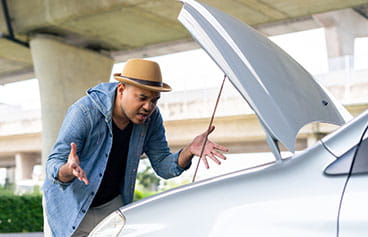 Frustrated African-American male standing next to a car with it's hood open with problems. 
