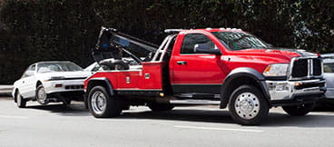 Red tow truck driving away with an attached gray sedan