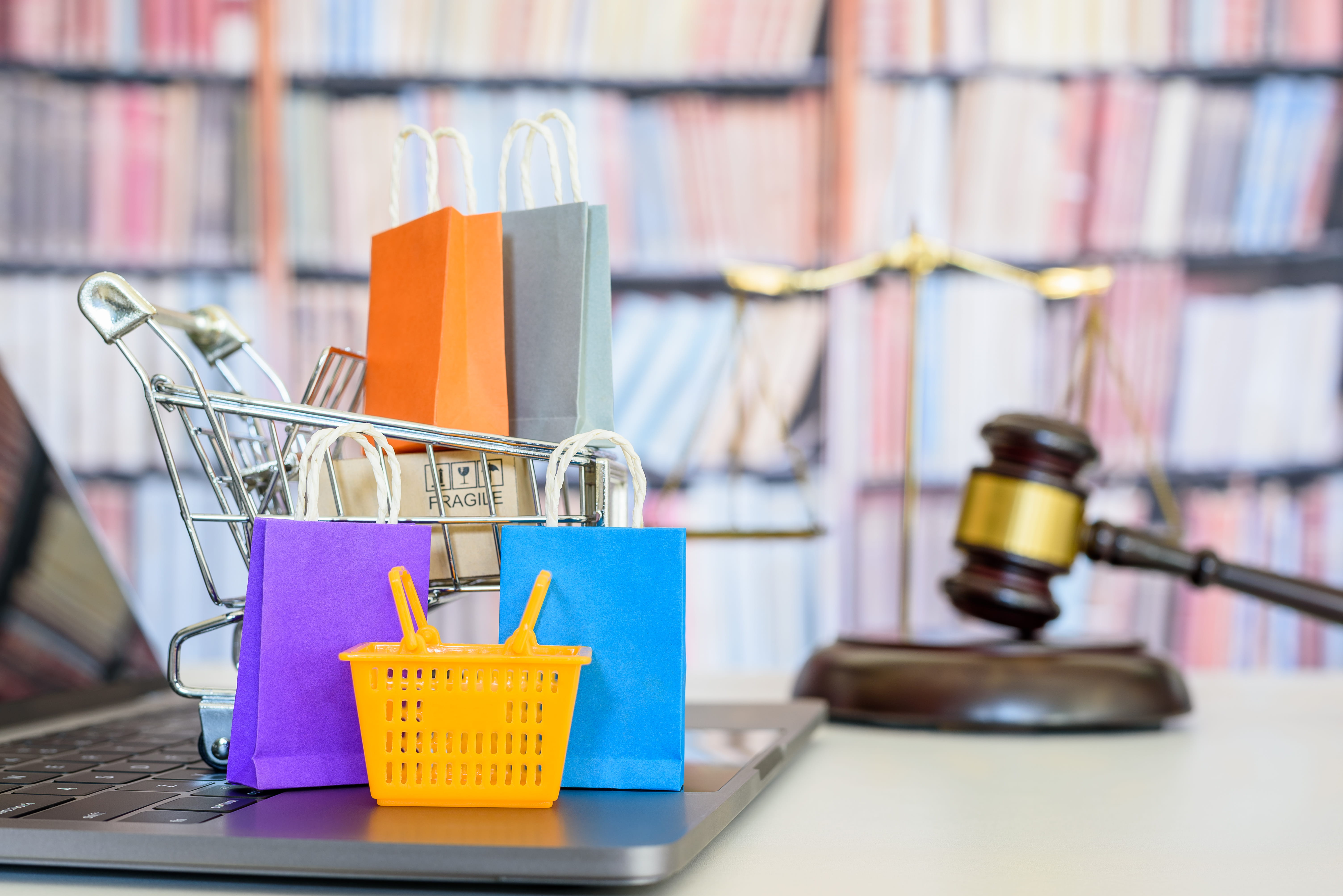 hopping basket, shopping bags and a shopping cart on a laptop computer with judge gavel, balance sale of justice and bookshelf 