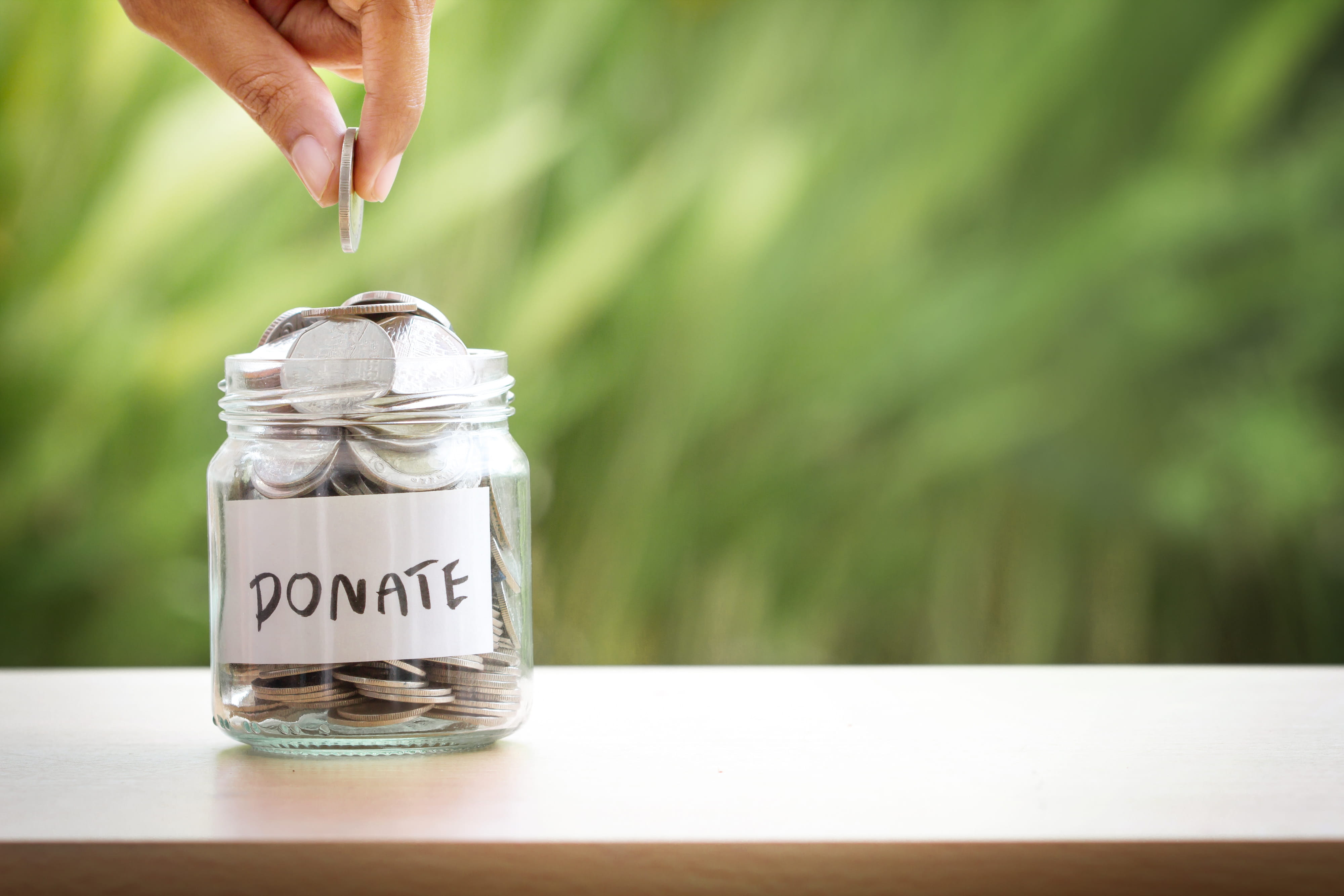 Hand putting Coins in glass jar for giving and donation