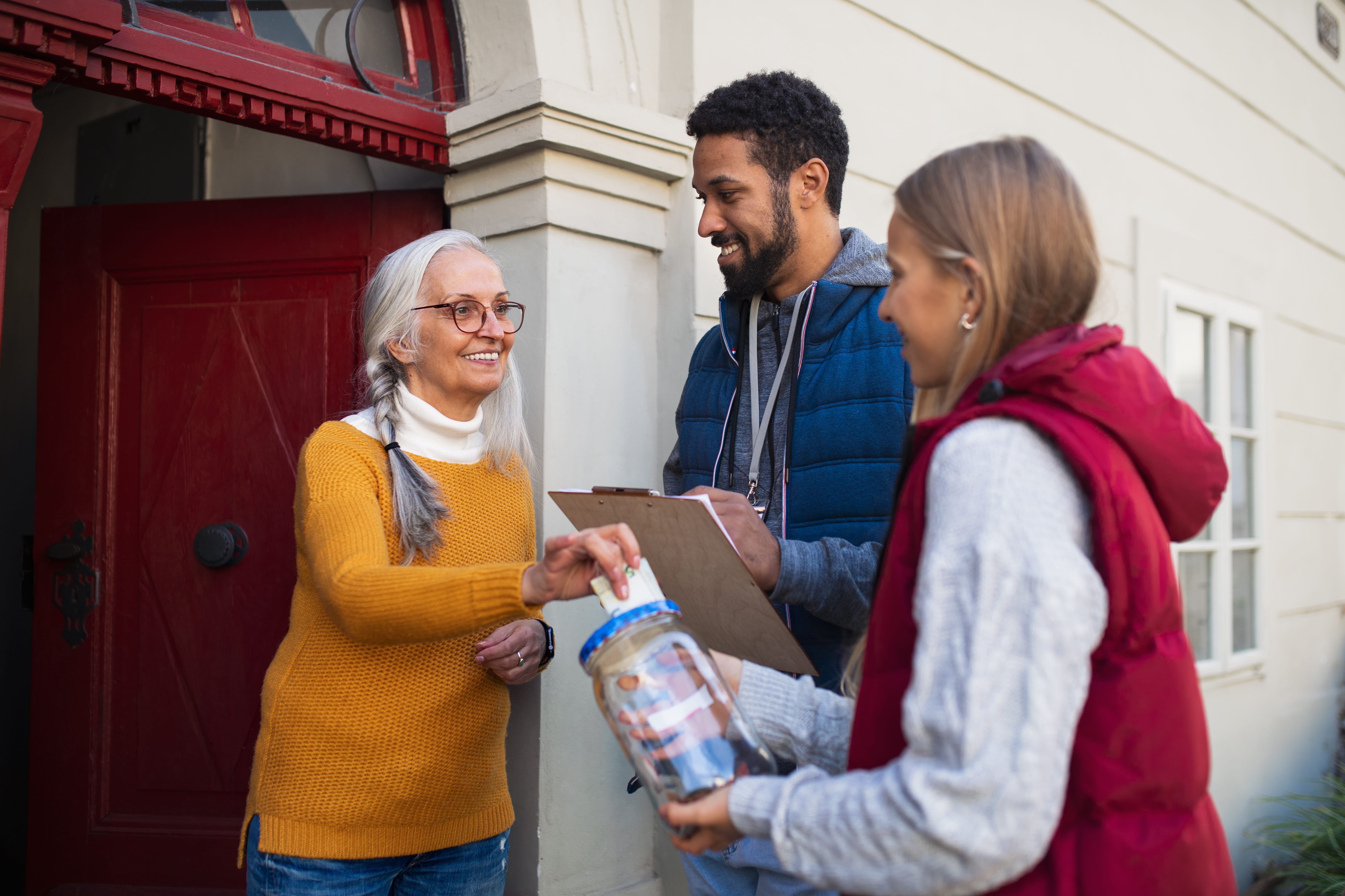 Young door to door fundraisers talking to senior woman and collecting money for charity in street