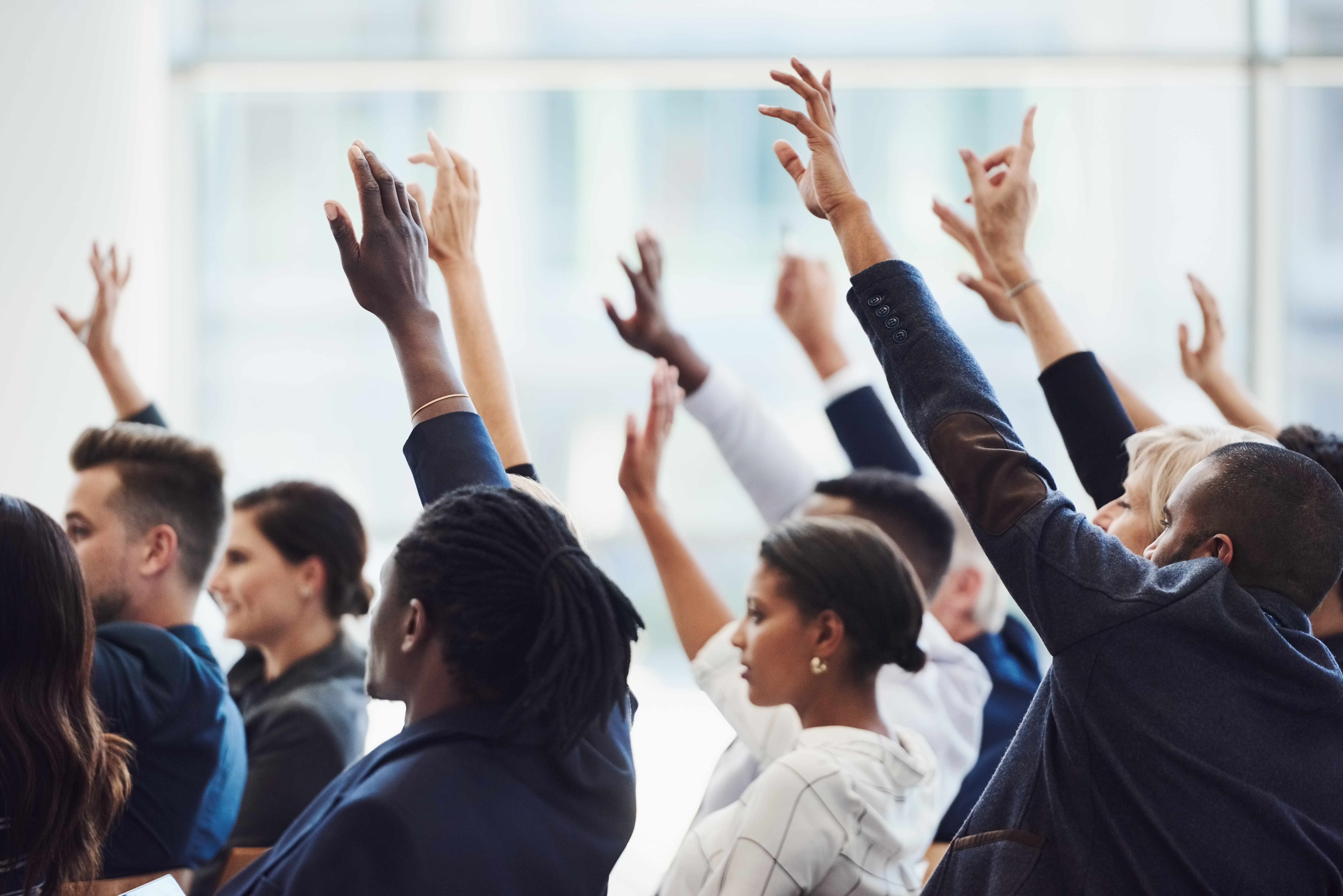 Diverse group of men and women with raised hands asking questions