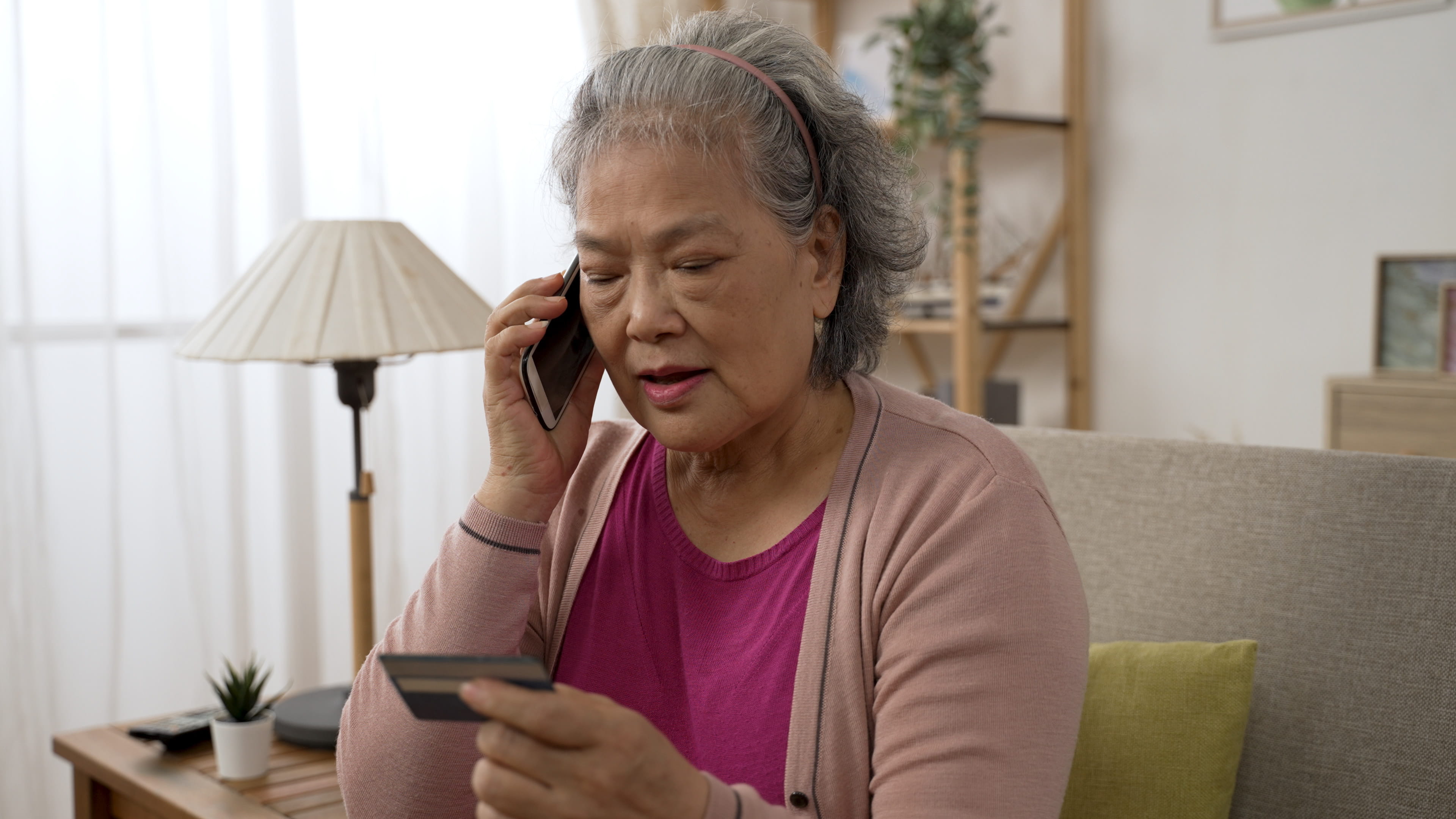 senior woman giving credit card details on the mobile phone in the living room at home