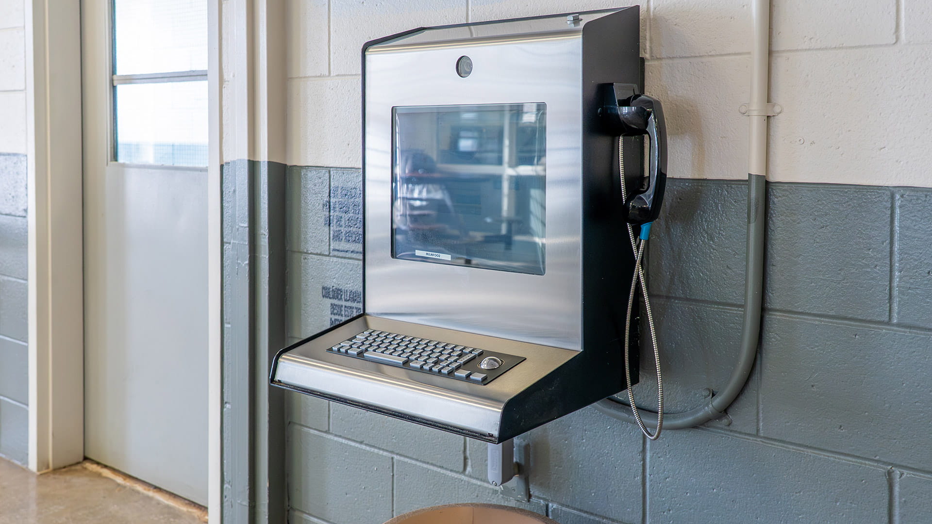 A telephone with a video screen attached to a wall inside of a prison.