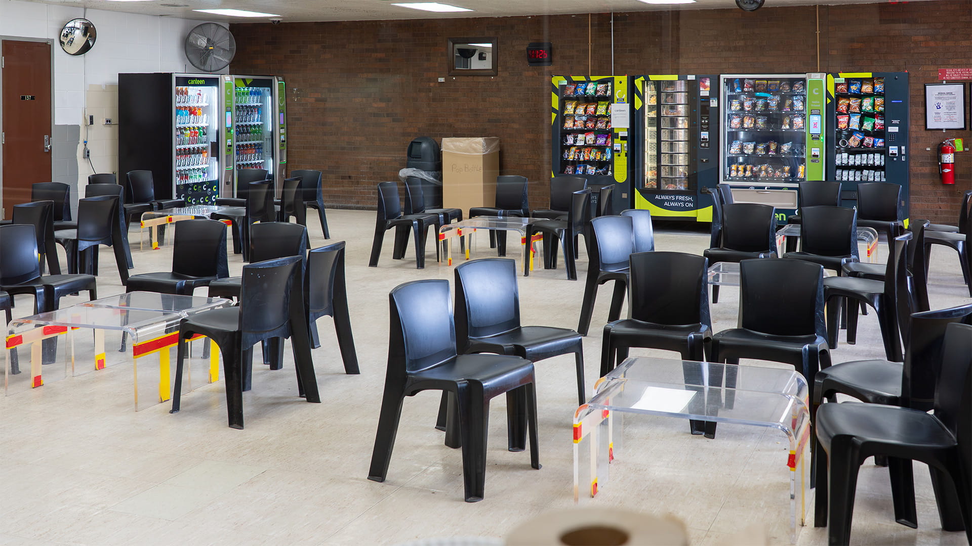 A prison visitation room with groups of chairs around small tables.
