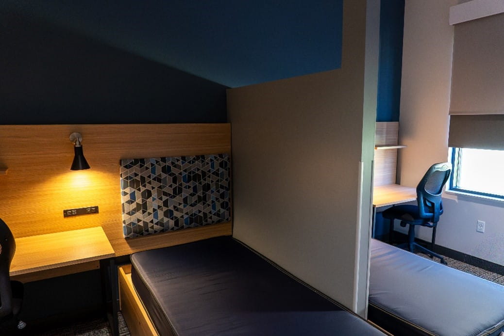 A dormitory with two twin beds and desks with office chairs.