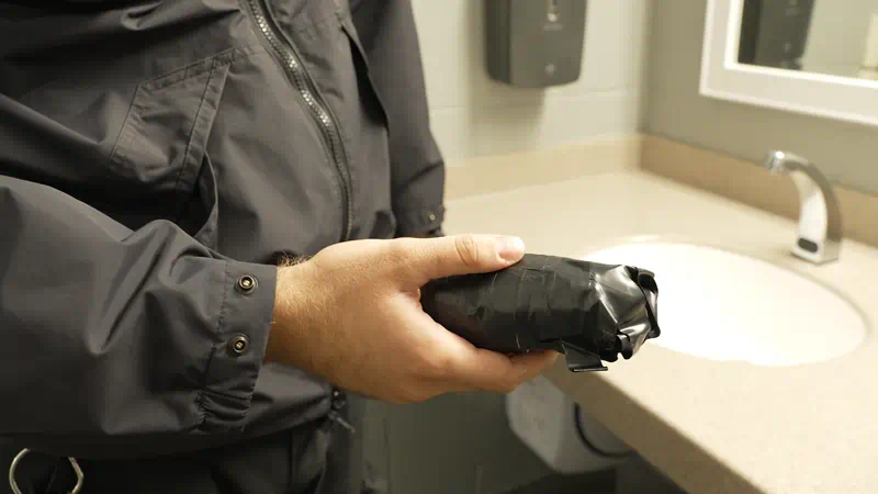 A male corrections officer's hand holding a cylinder-shaped object wrapped in electrical tape.