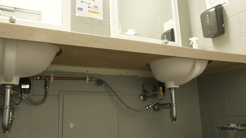 The underside of two public restrooms sinks with two mirrors above the sinks.