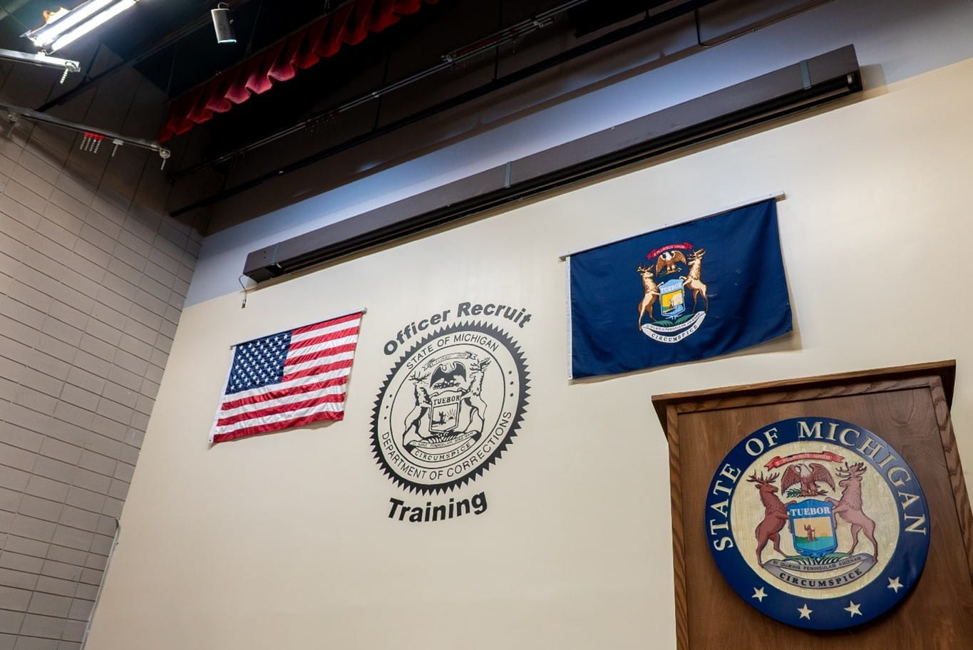 A wall with the Michigan Department of Corrections seal and text reading "Officer Recruit Training" with a podium in the foreground.