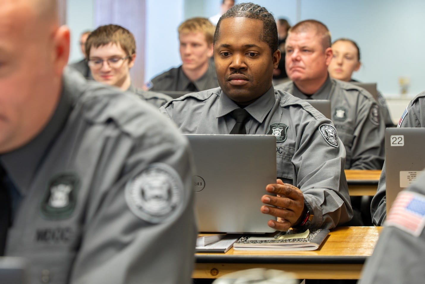A corrections officer recruit sits at a desk while working on a laptop.