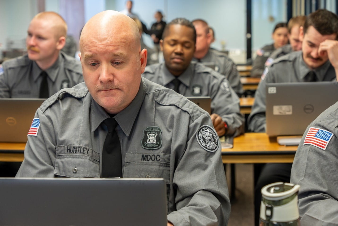 Corrections officer recruits seated at tables and working on laptops.