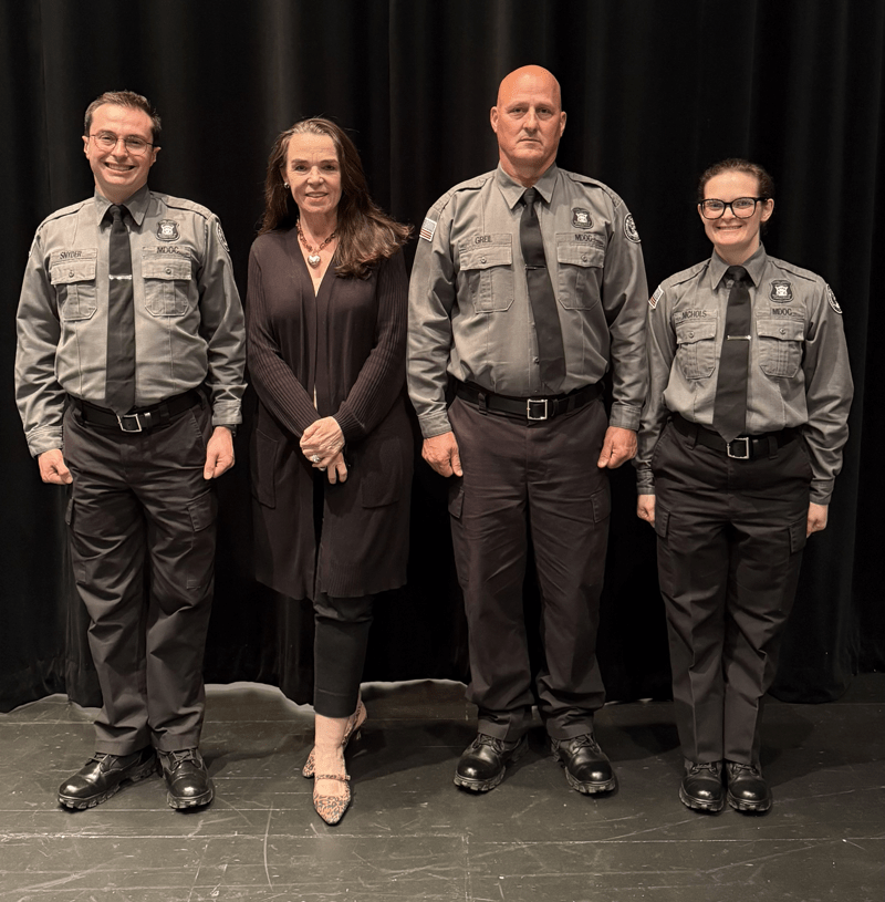 Michigan Department of Corrections Director Heidi E. Washington stands between three new corrections officer recruits.
