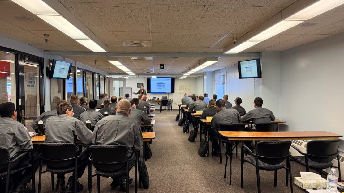 Corrections officer recruits seated in a classroom all looking forward and listening to an instructor.