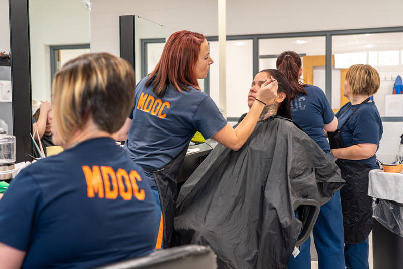 Female prisoners practicing cutting hair and applying cosmetics to other women in a classroom salon.