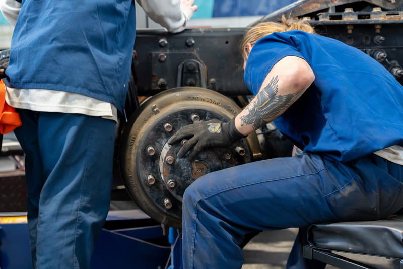 A male prisoner assisting another male prisoner with attaching a wheel drum to a vehicle.