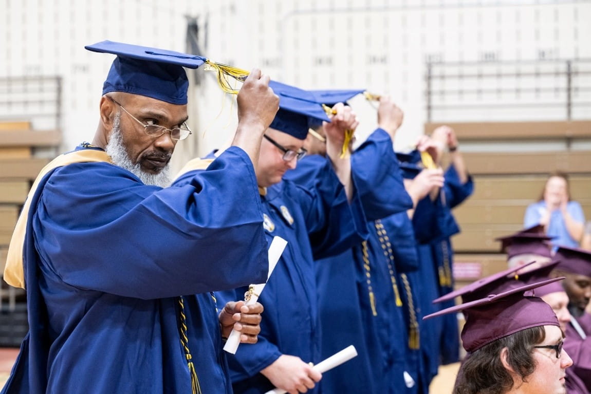 Recent college graduates in their caps and gowns, moving their tassels across their mortarboard hats