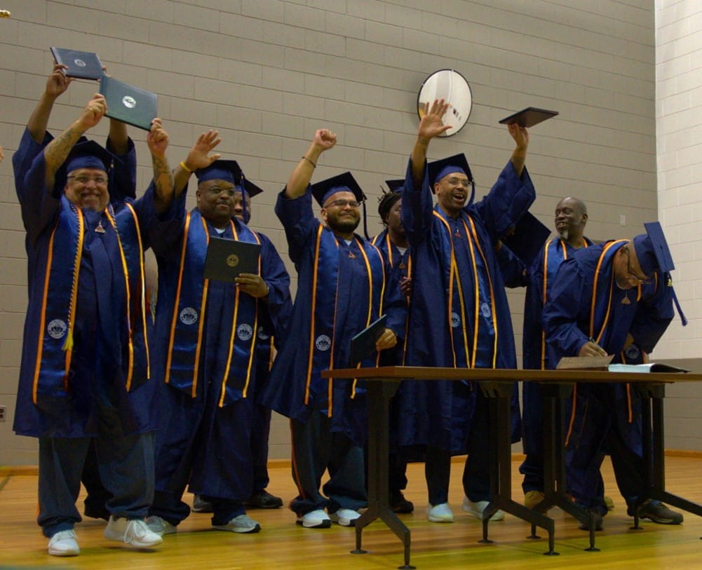 Recent college graduates in their caps and gowns raising their diplomas above their heads