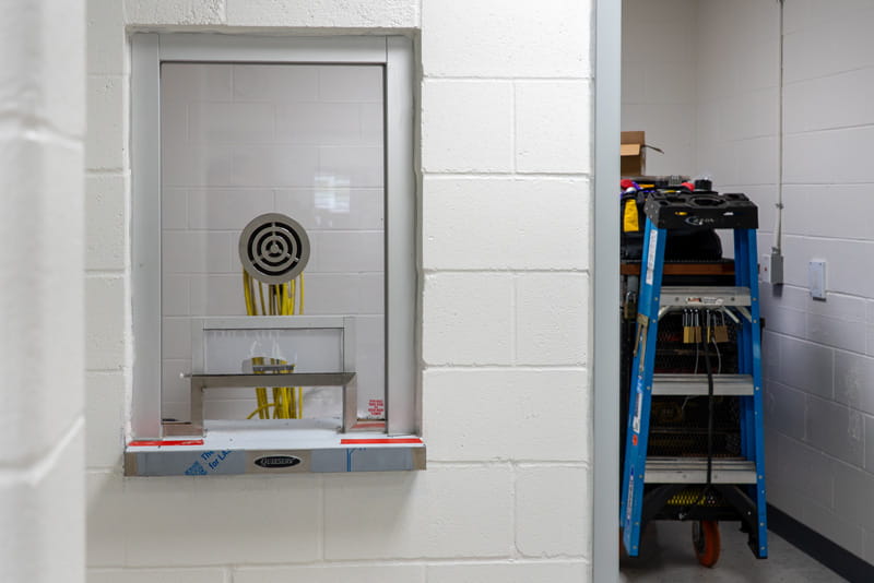 A window with a speaker on a corner and a ladder in the background.