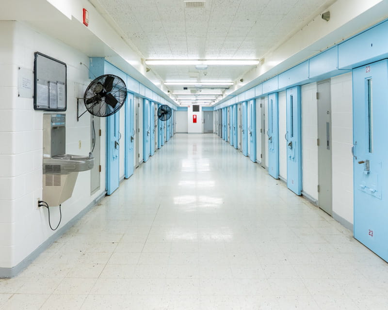 A hallway in a prison with multiple cell doors on each side.