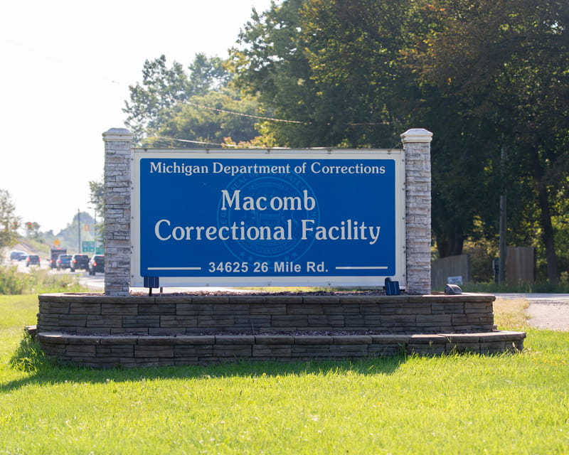 A sign that reads "Macomb Correctional Facility" on a grass lawn.
