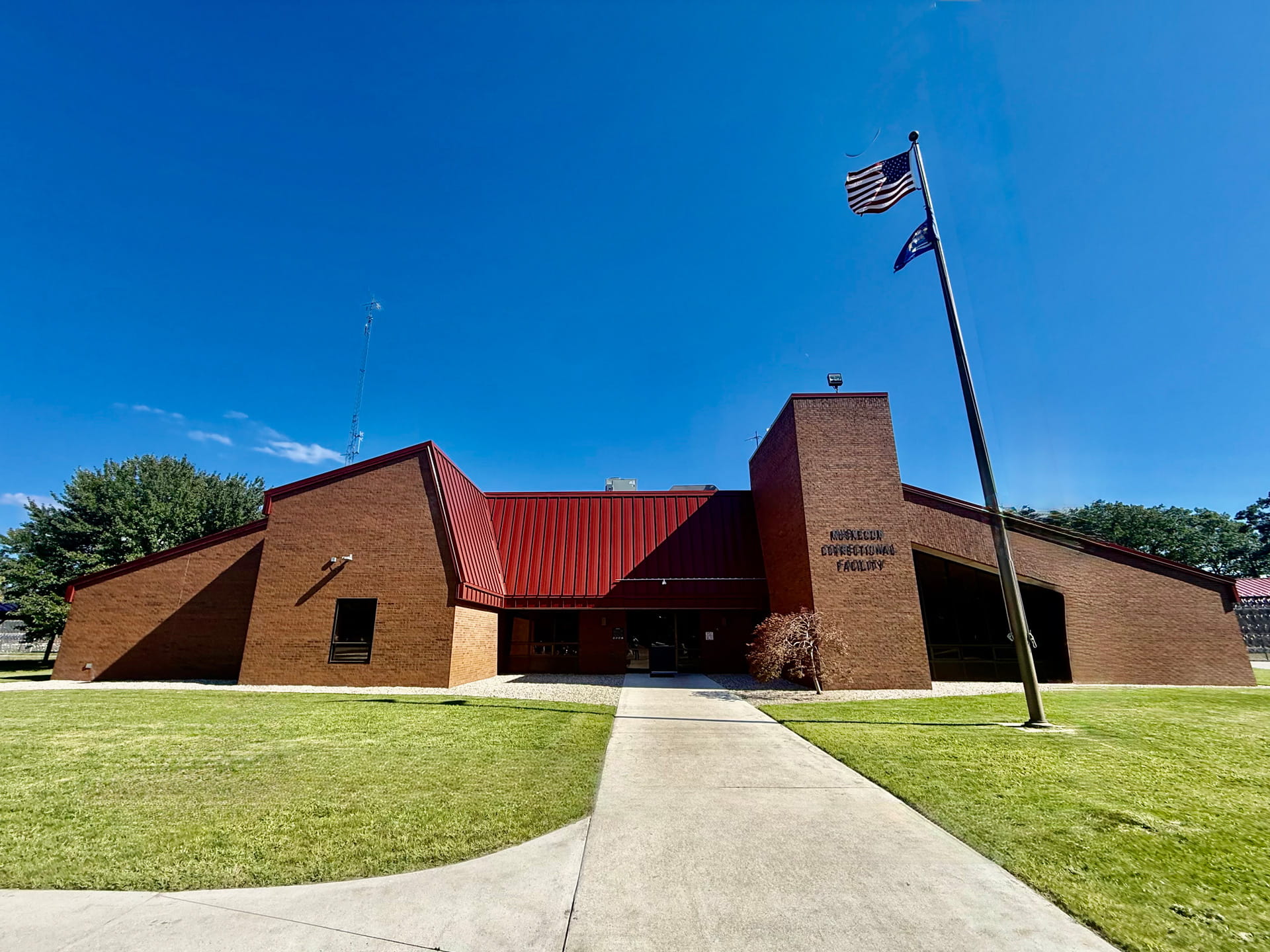 Main entrance to a building with a flagpole, a green lawn, and a cloudless blue sky in the background.
