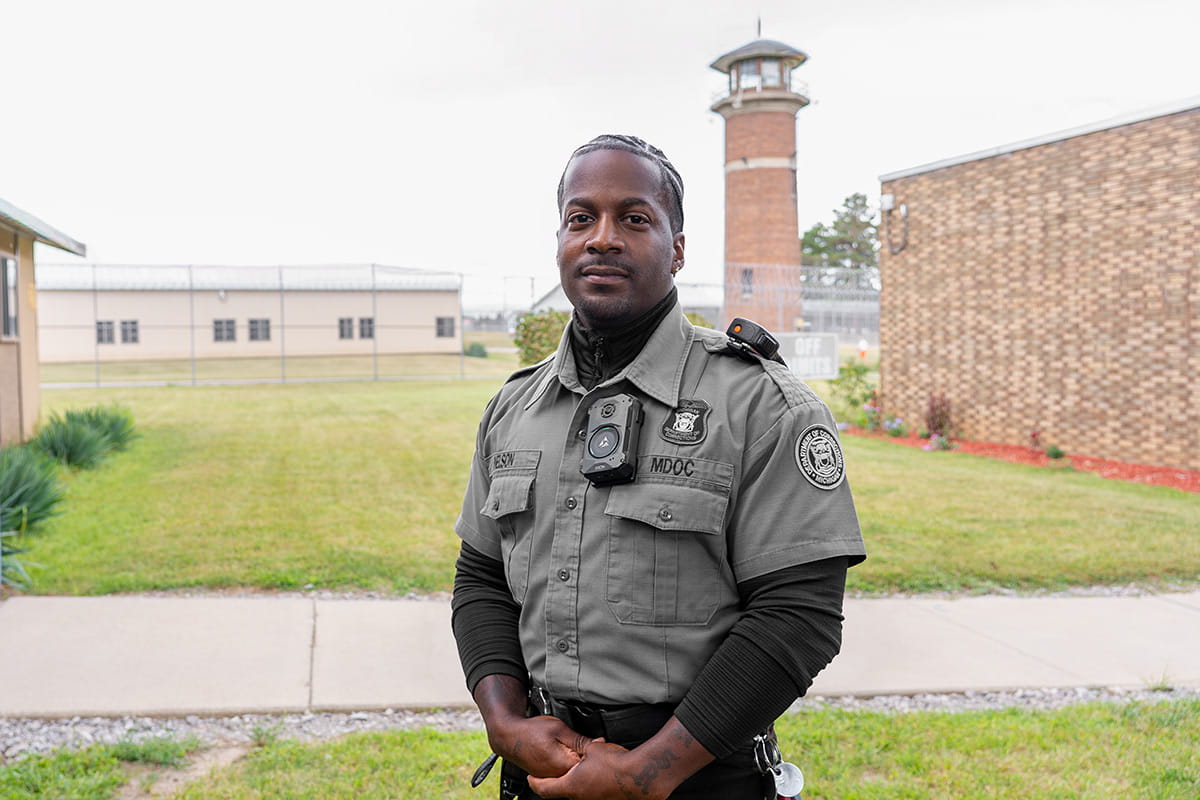 A man suited in his corrections officer uniform and standing in the yard of a prison.