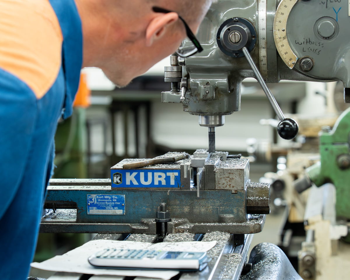A prisoner wearing safety glasses keeping watch on a drill press.