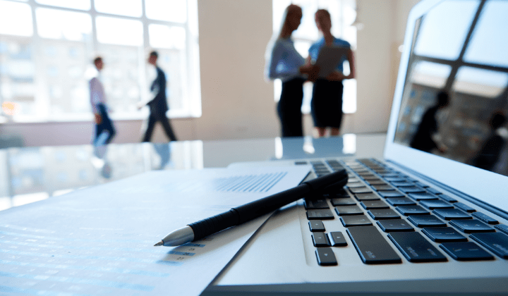 Pen and form laying on a laptop with people in the background