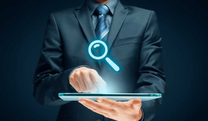 Man in a suit holding a tablet with a magnifying glass icon floating about tablet