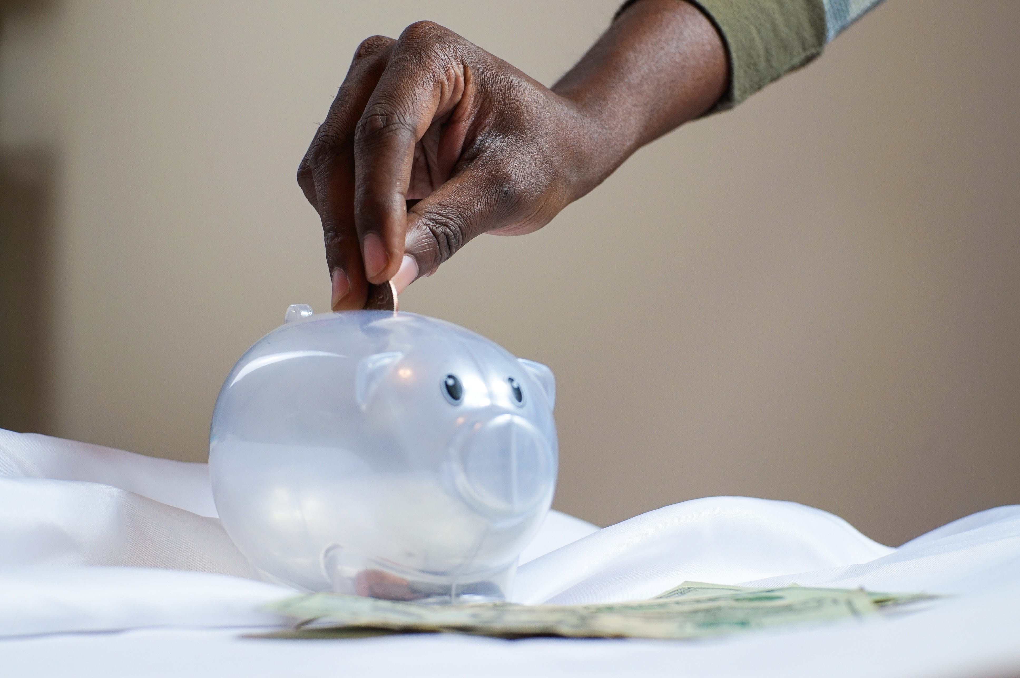 image of a hand putting a coin in a piggy bank with coins all around