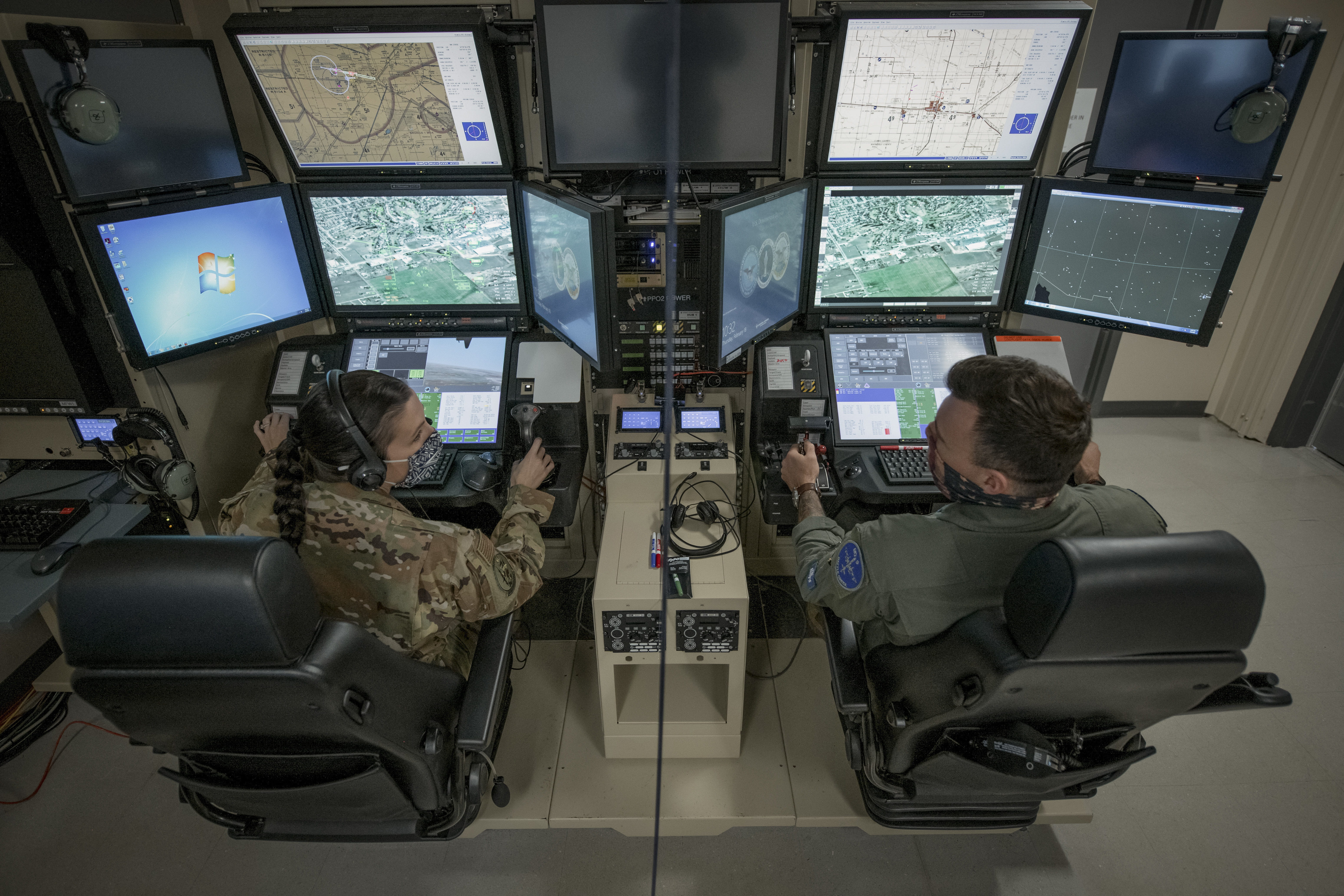 Two Ming pilots sit in chairs looking at data on multiple monitors