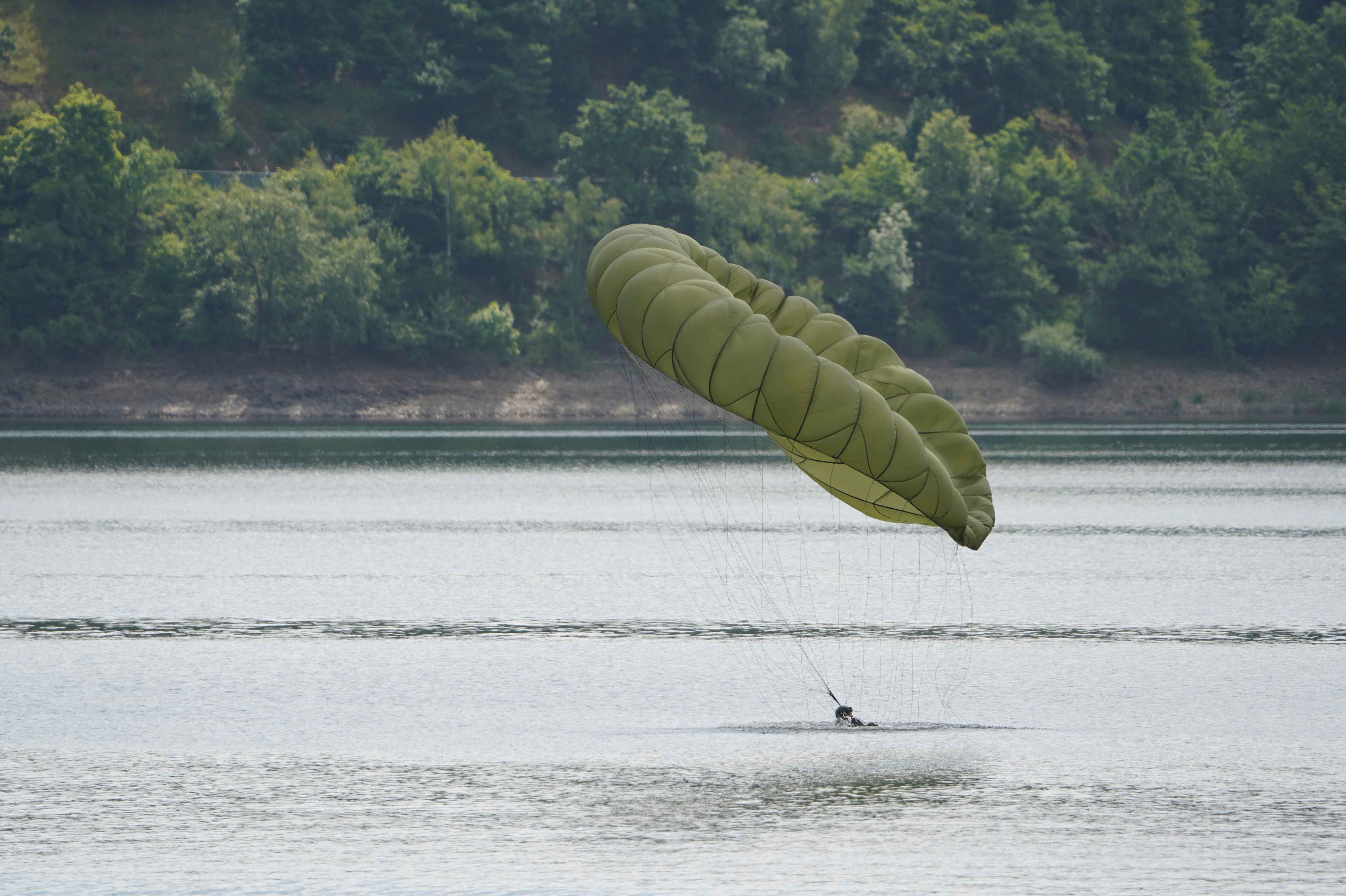 soldier with a deployed parachute enters the water