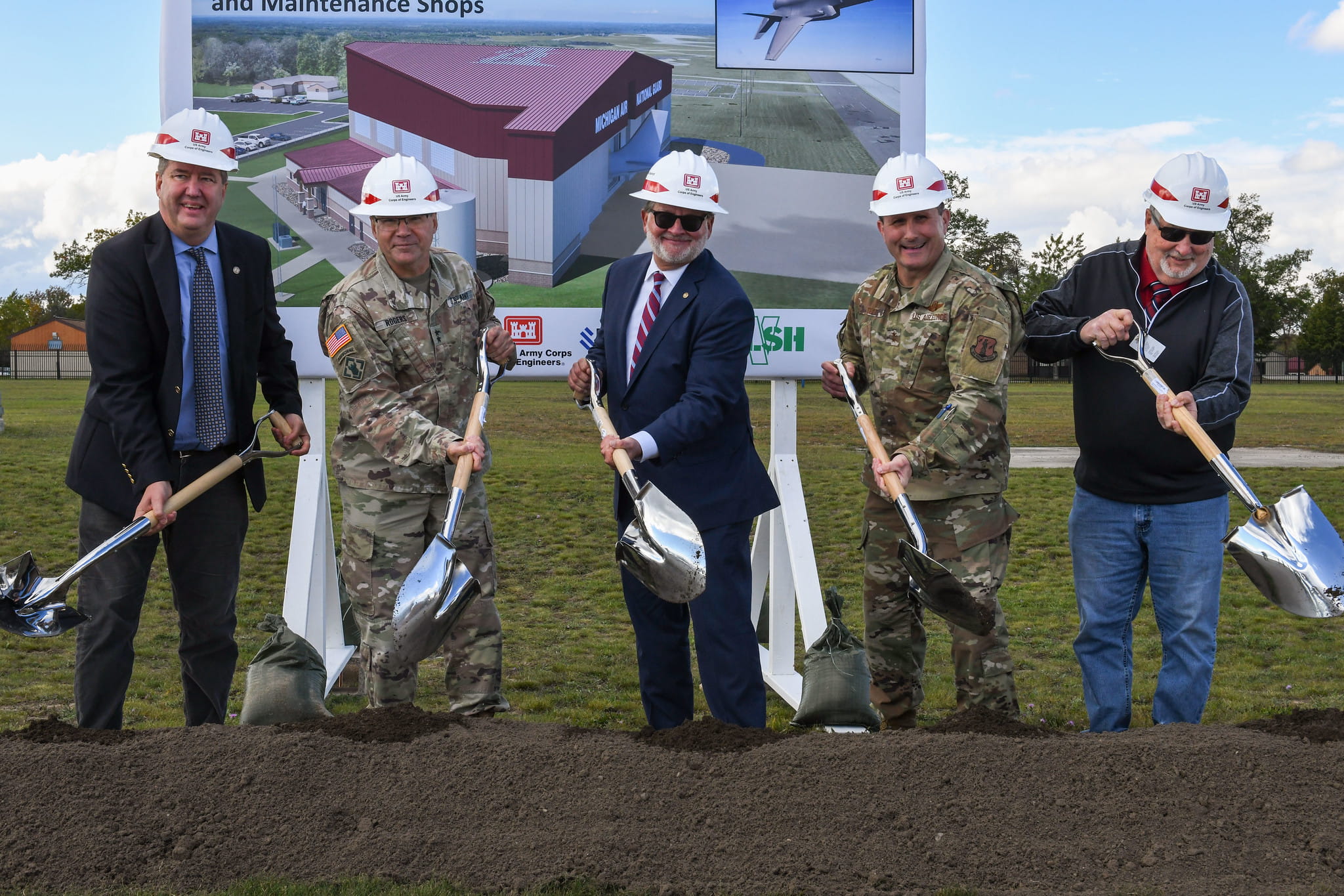 light-skinned men wearing hardhats shoveling dirt at ceremony
